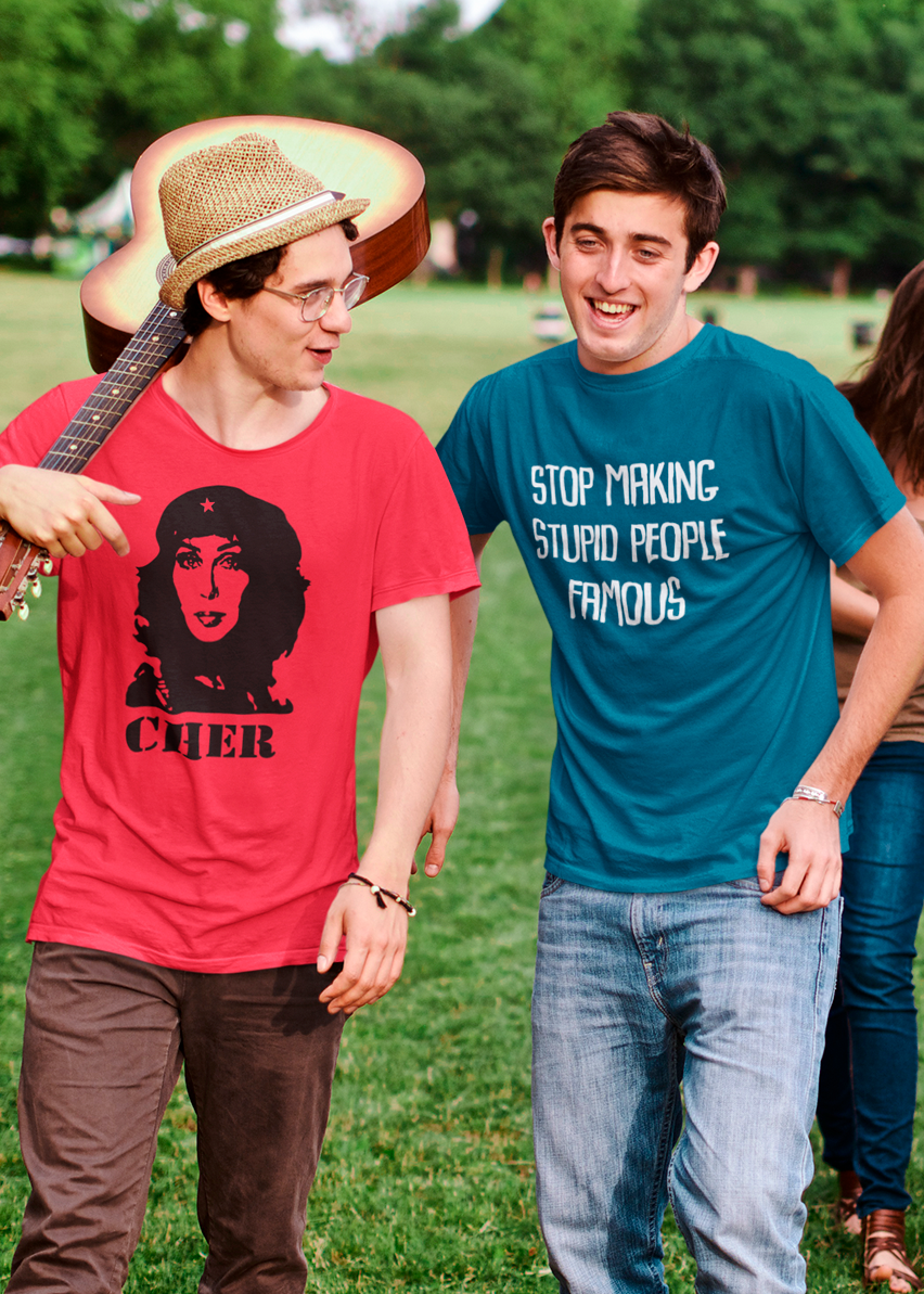 Two young men at a festival in custom t-shirts, one  with a portrait print and the word 'CHER' below it the other has a slogan that reads 'Stop Making Stupid People Famous'